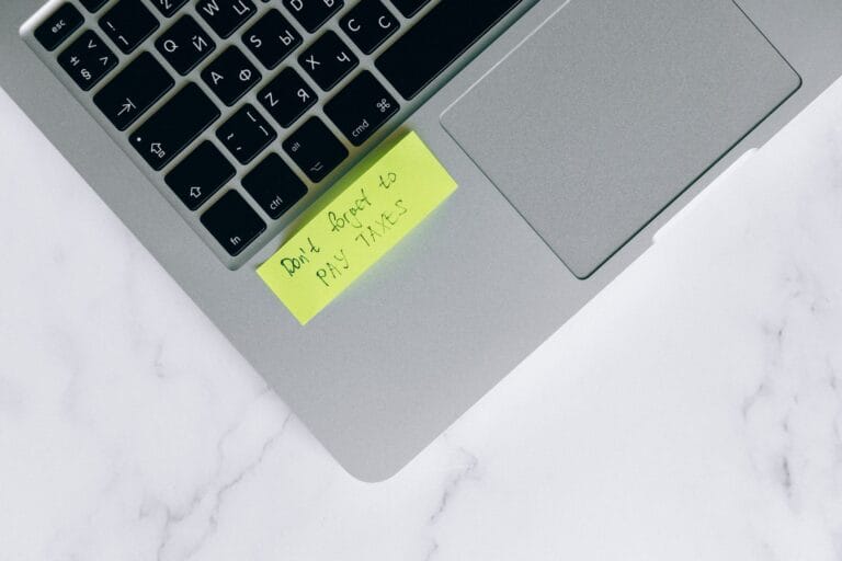 Żółta karteczka z przypomnieniem o podatkach przyklejona do laptopa