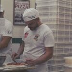 Pizzaiolo rozsmarowuje sos na cieście w kuchni pizzerii w Neapolu
