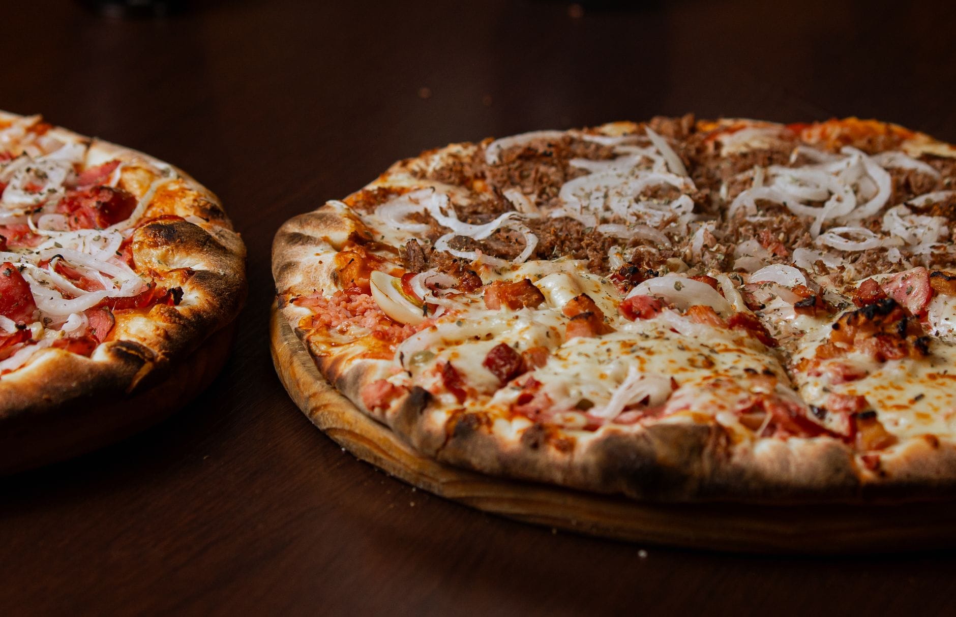 Dwie pizze z pepperoni i cebulą na drewnianym stole