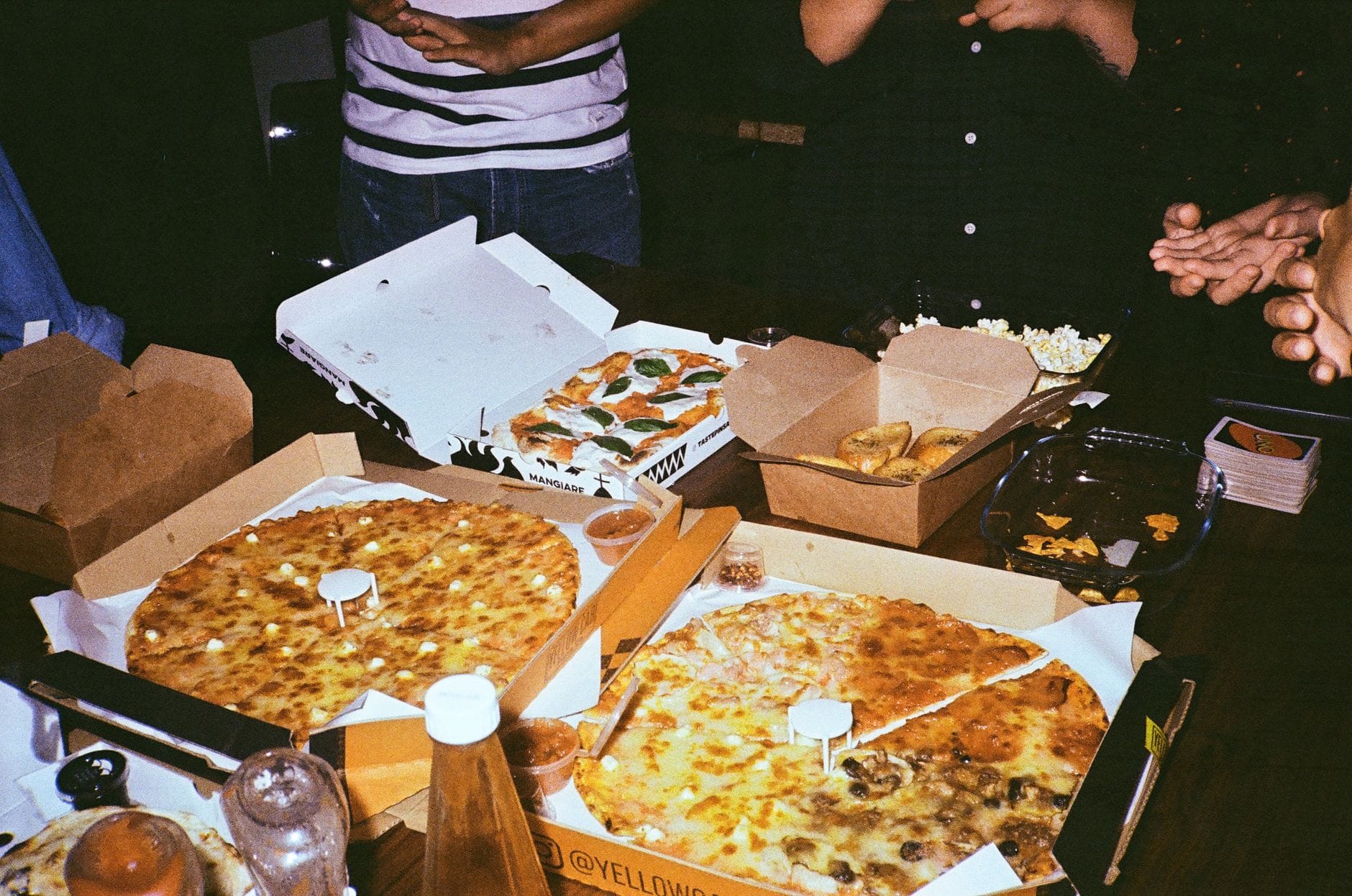 Goście na domowym przyjęciu jedzą pizzę i przekąski przy stole