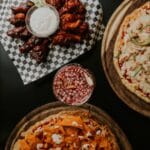 Kulinarne party z pizzą jak dobrać ilość ciasta i dodatków na gości Pizze i skrzydełka z napojem na imprezowym stole do dzielenia się