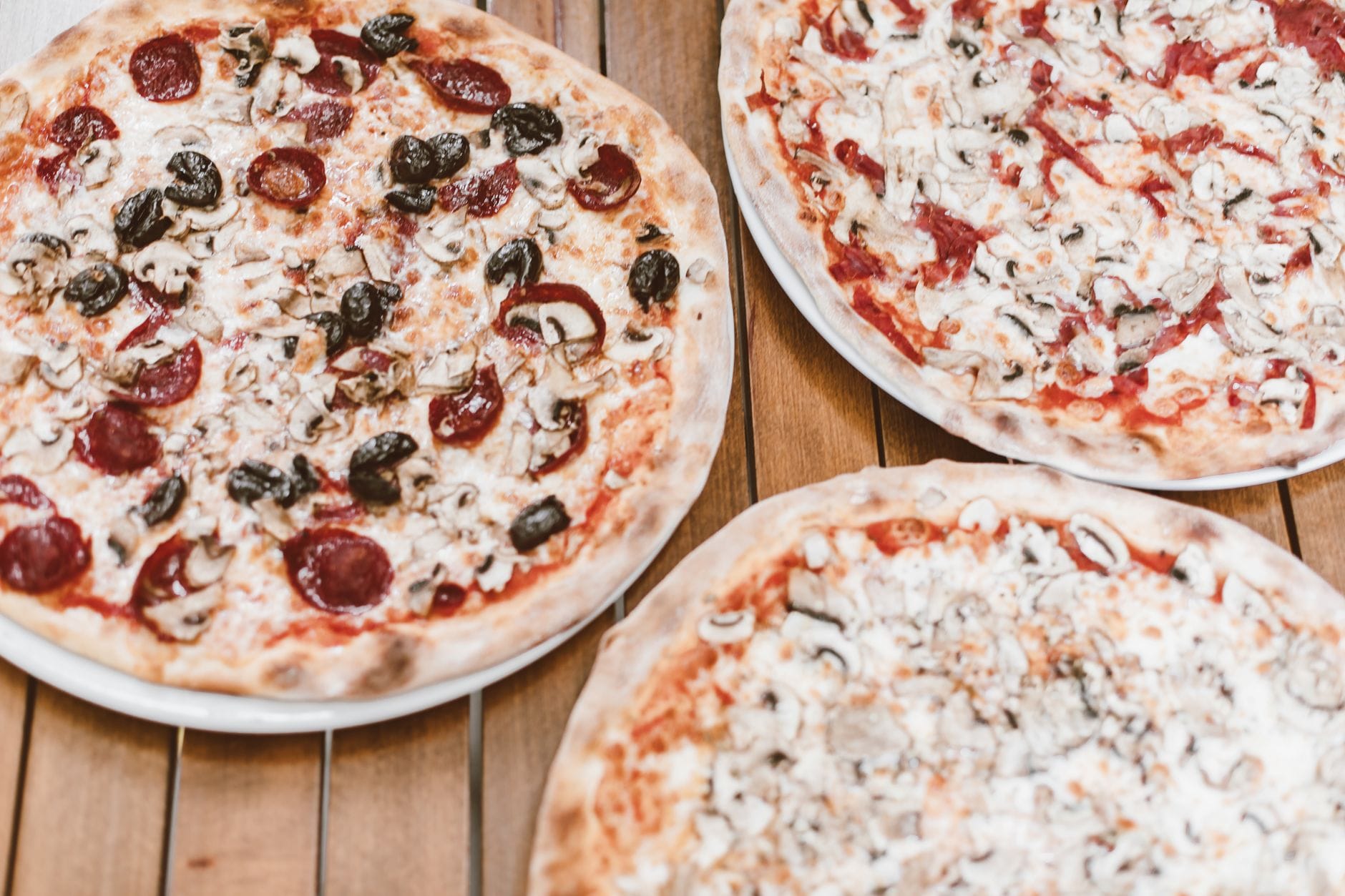 Trzy pizze z pieczarkami i pepperoni na drewnianym stole