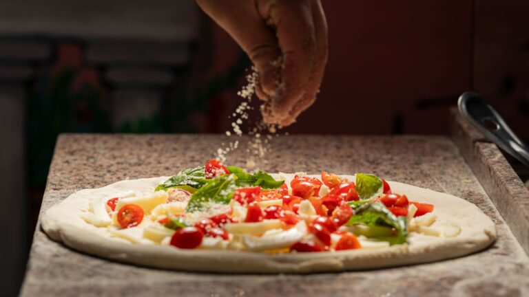 Kucharz posypuje pizzę serem z pomidorami i świeżą bazylią