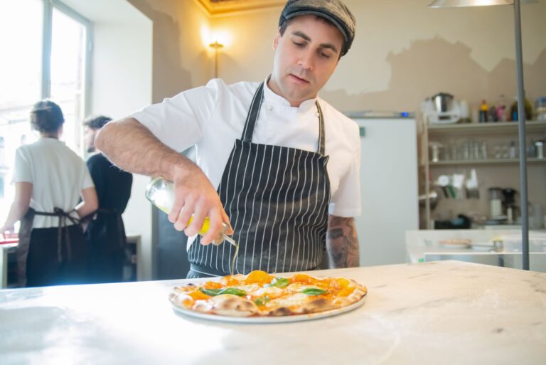 Kucharz skrapia oliwą świeżo upieczoną pizzę w jasnej kuchni