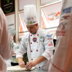 Pizzaiolo w czapce kucharskiej przygotowuje ciasto na pizzę gourmet